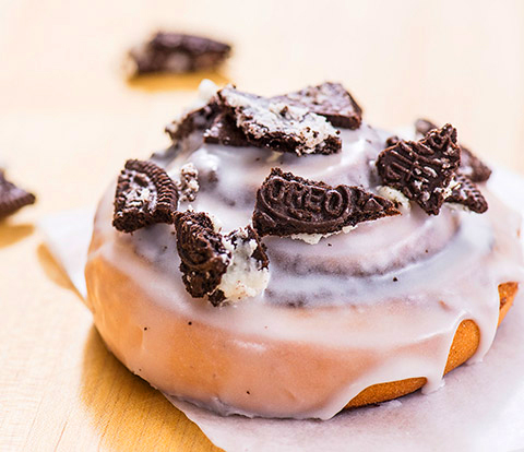 A cinnamon roll covered with white icing and OREO Cookie Pieces.